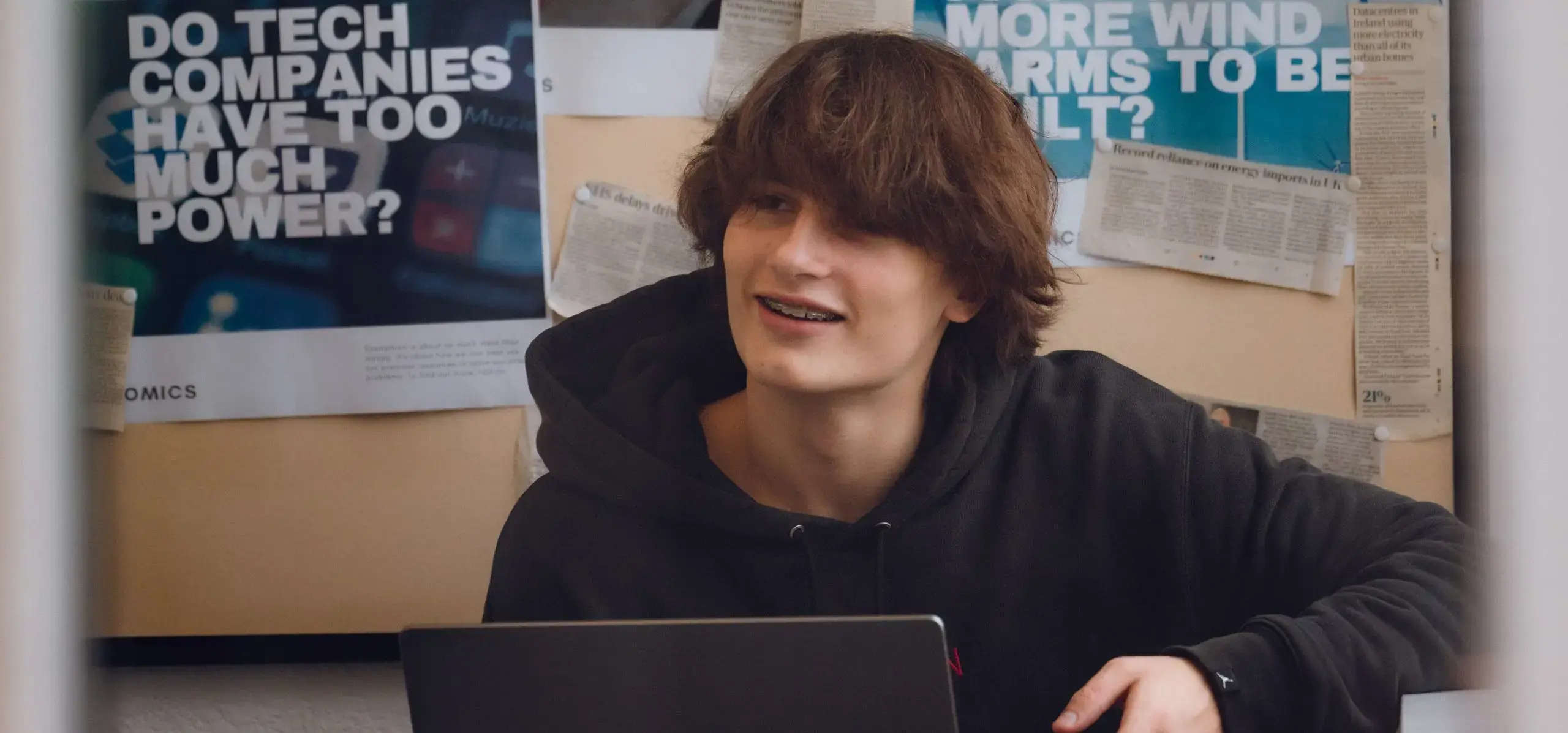 Student in class, smiling while holding a laptop