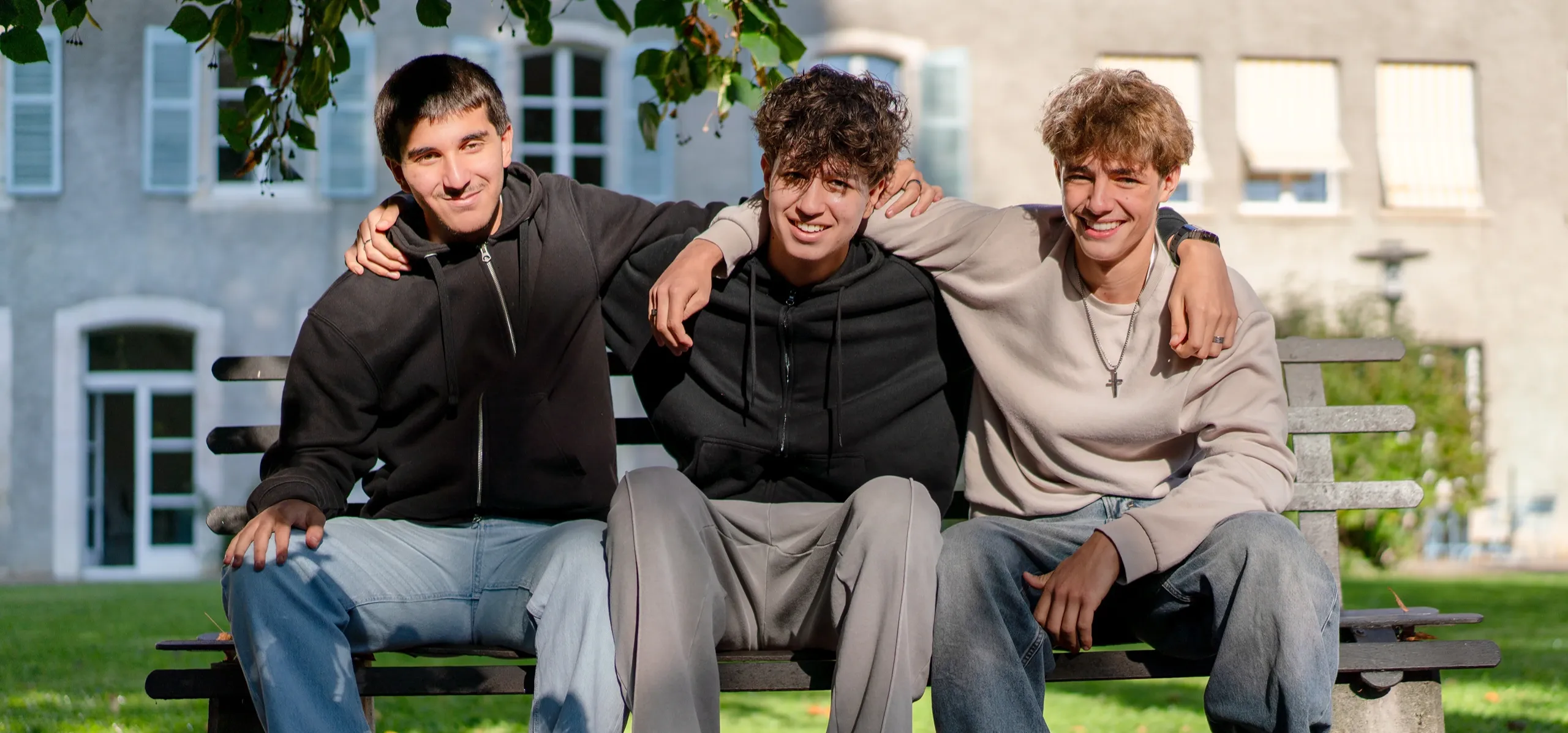 Three students smiling together sitting on a bench on campus
