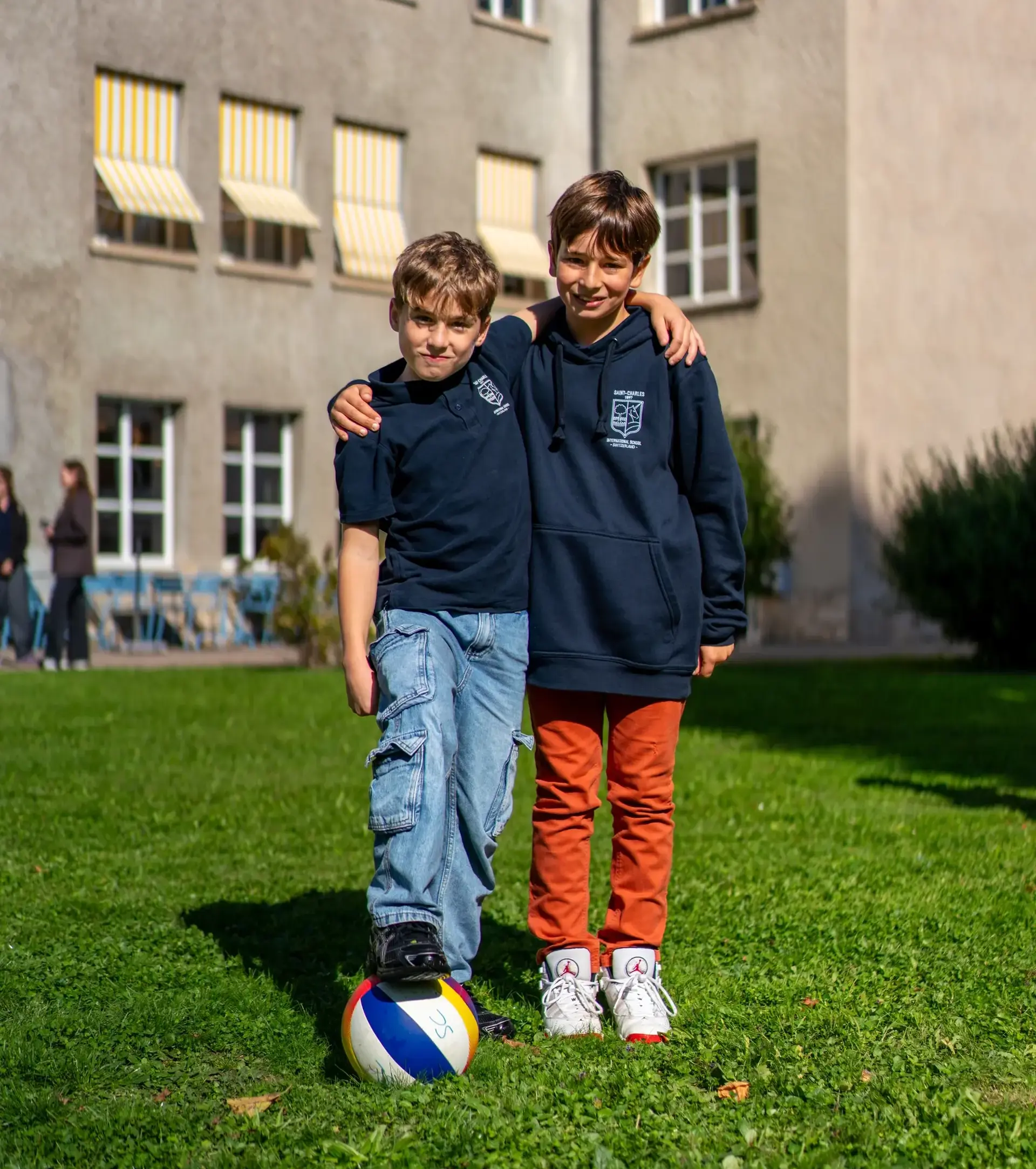 Two students with their arms around each other, smiling, with one foot on a football.